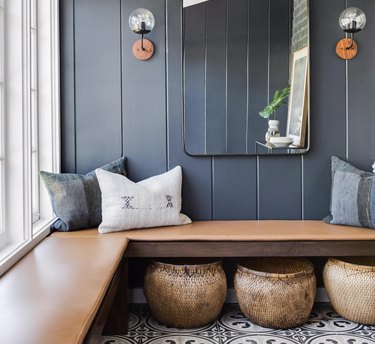 family room storage with wood bench, gray walls, large mirror, matching glass sconces, throw pillows and large baskets with bold pattern tile floors.