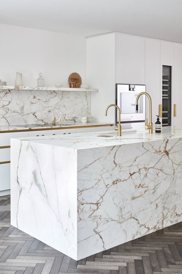 wraparound marble kitchen island with gold veining and brass faucets