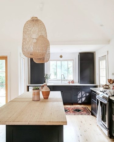 masculine boho decor in white kitchen with black cabinets and cane pendants