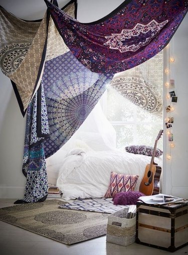 Boho bedroom with draped tapestries by white bed
