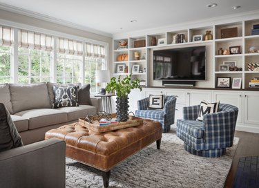 transitional family room with plaid side chairs, leather tufted ottoman, flat screen tv, built in shelves.