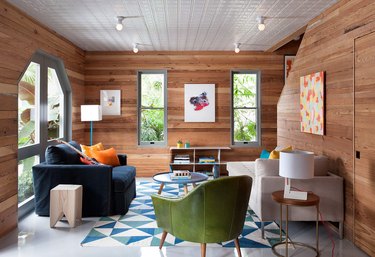 transitional family room with overstuffed and modern sofas, green side chair, blue patterned rug, wood paneled walls, art.