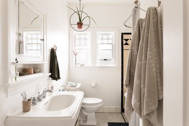 white bathroom with pedestal sink, toilet and hanging towels