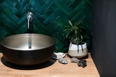 green herringbone tile backsplash, black vessel sink with silver wall-mounted faucet, wood bathroom vanity top, vase with succulent