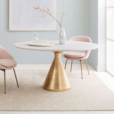 Minimalist dining room idea with white marble oval dining table with brass pedestal and blush midcentury chairs