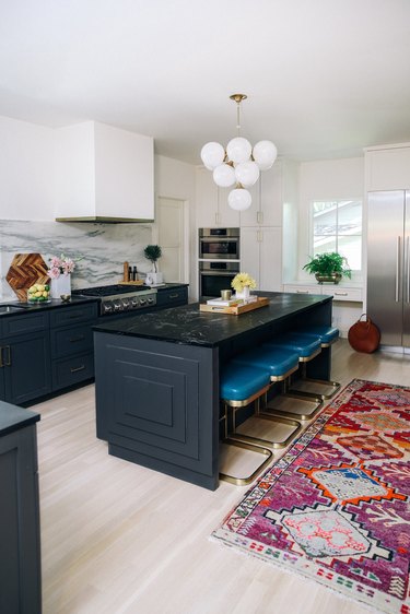 black marble kitchen island with teal barstools and printed kitchen rug