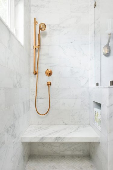 marble bathroom with brass fixtures and shower storage ideas and shower bench