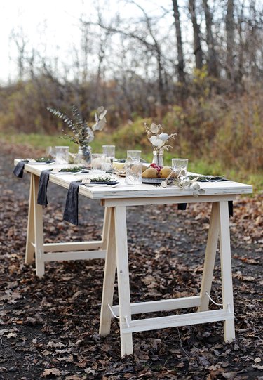 DIY minimalist table with wood top and sawhorse legs set up in forest