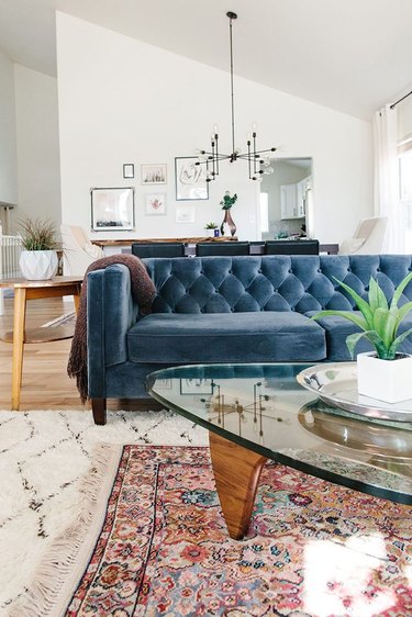 living room with blue tufted sofa and layered area rugs