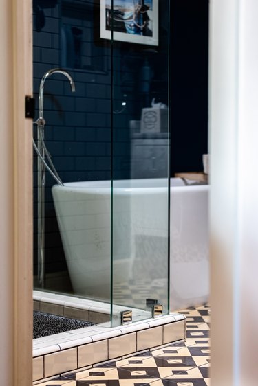 freestanding white tub with a floor-mounted faucet, blue wall, black and white tiled floor, glass shower door