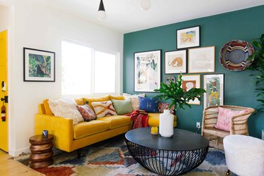 A living room with green walls, a mustard couch, and red accents