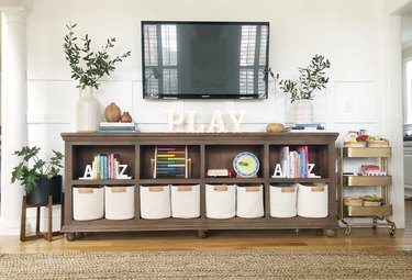 Family room toy storage in shelf under TV and white rope bins