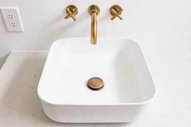 white ceramic vessel sink with gold stopper and wall-mount faucets, outlet