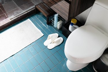 bathroom toilet, blue-tiled floor, bath mat and slippers