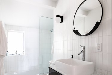 white bathroom with shower, circular mirror and bathroom sink