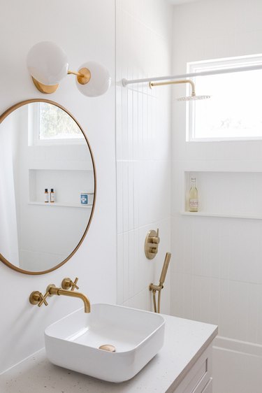 shower/tub combo, bathroom sink, circular mirror and brass fixtures