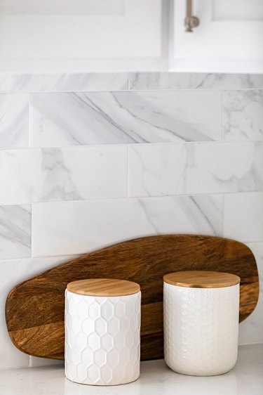 close up view of marble tile backsplash, cutting board and two white decorative jars