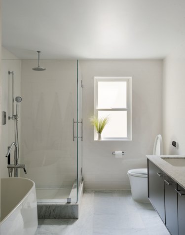 large bathroom, wood floating vanity, white toilet, glass shower with overhead showerhead, tan tile and wall color