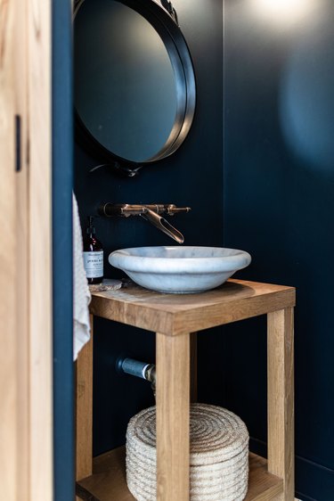 deep blue walls, round mirror with black trim, vessel sink with gold faucet, wood vanity countertop