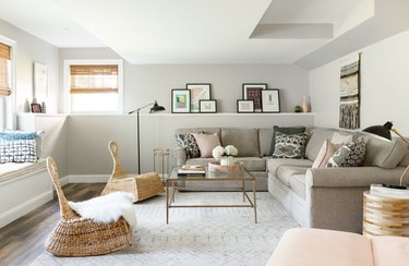 basement lighting in basement with beige sectional couching, wicker side chairs, square coffee table, photos and art on built in shelf, black floor lamp, black reading lamp.