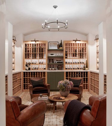 basement lighting in basement wine cellar with natural wood shelves, four leather wing back chairs, wood coffee table, and chandelier