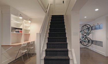 basement lighting in white basement with staircase, work area with built in shelves, two chairs, white sconces, and recessed lighting