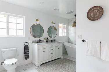 bathroom with double-sink vanity, two circular mirrors, stand-alone tub and toilet