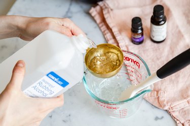 person pouring isopropyl rubbing alcohol into gold measuring cup over pyrex measuring cup