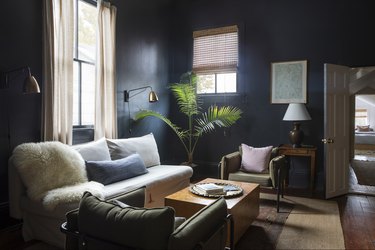 a sitting area with the walls painted a moody black, a white couch, green mid-century arm chairs, and a solid wood coffee table