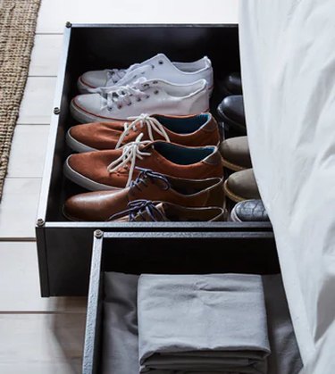 IKEA bedroom idea with a black shallow rolling boxes peeking out from under a bed, one has shoes in it, the other has sheets