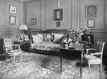 black and white photograph of a living room space with chairs, couch, and framed artworks