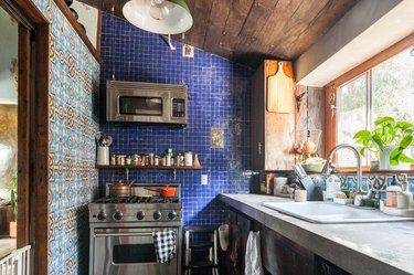 kitchen with wood-paneled slanted roof, stainless steel microwave and oven and blue tile backsplash