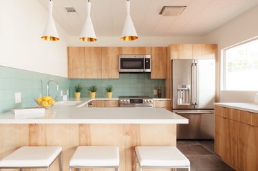 view of a kitchen with mint green tile backsplash, kitchen island and three pendant lights