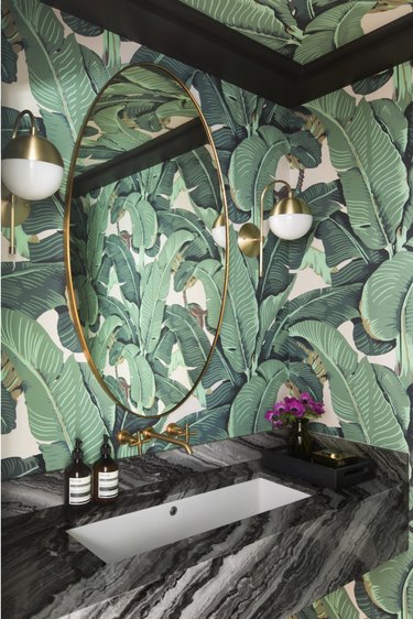 bathroom mirror lighting ideas with gold sconces and botanical print wallpaper