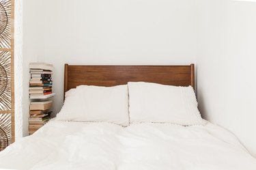studio bedroom idea with a modern wood headboard against a white wall, with a stack of books to the left
