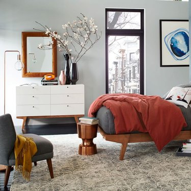modern studio bedroom idea with light gray walls, a mid-century-style wood bed with gray and rust bedding, and a white mid-century style dresser