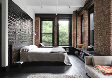 modern loft bedroom with exposed brick, dark floors, and low shelving