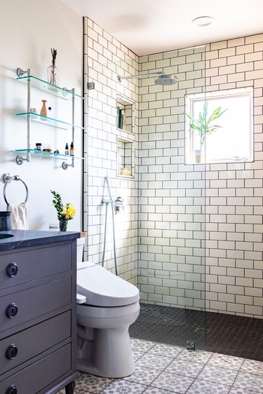 bathroom with shower with subway tile walls, glass wall, toilet and grey bathroom vanity with sink