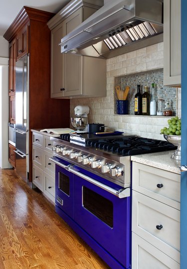 travertine kichen backsplash in kichen with a blue stove and multi-tone cabinets