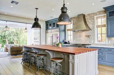 travertine backsplash in traditional industrial kitchen with butcher block island and blue cabinets