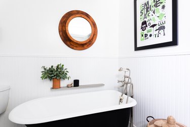 black clawfoot bathtub, white wainscoting, round mirror with wood trim