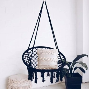 black hanging boho chic chair with fringe white pillow and plant