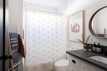 white shower curtain, ladder with towels hung, round wooden mirror, black and white bath vanity