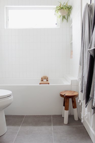 guest bathroom idea with a small rustic wooden stool with white-dipped legs next to a white bathtub
