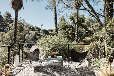 A second-story gravel patio with two black butterfly chairs, all surrounded by many trees