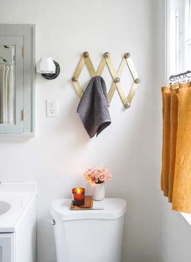 guest bathroom idea with a brass accordion peg rack hung over a toilet in a small white bathroom