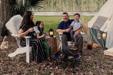 Family of four sitting in Adirondack chairs around the fire pit