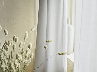 light gray curtains near dried plants and a white vase
