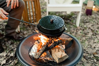 Enamel popcorn popper being held over fire pit flame