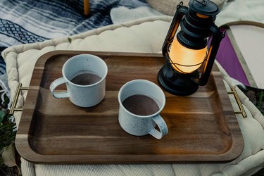 Two enamel camping mugs with hot cocoa on a tray with lantern